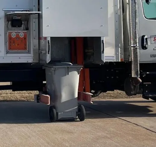 The truck's lift raising a bin toward the hopper.