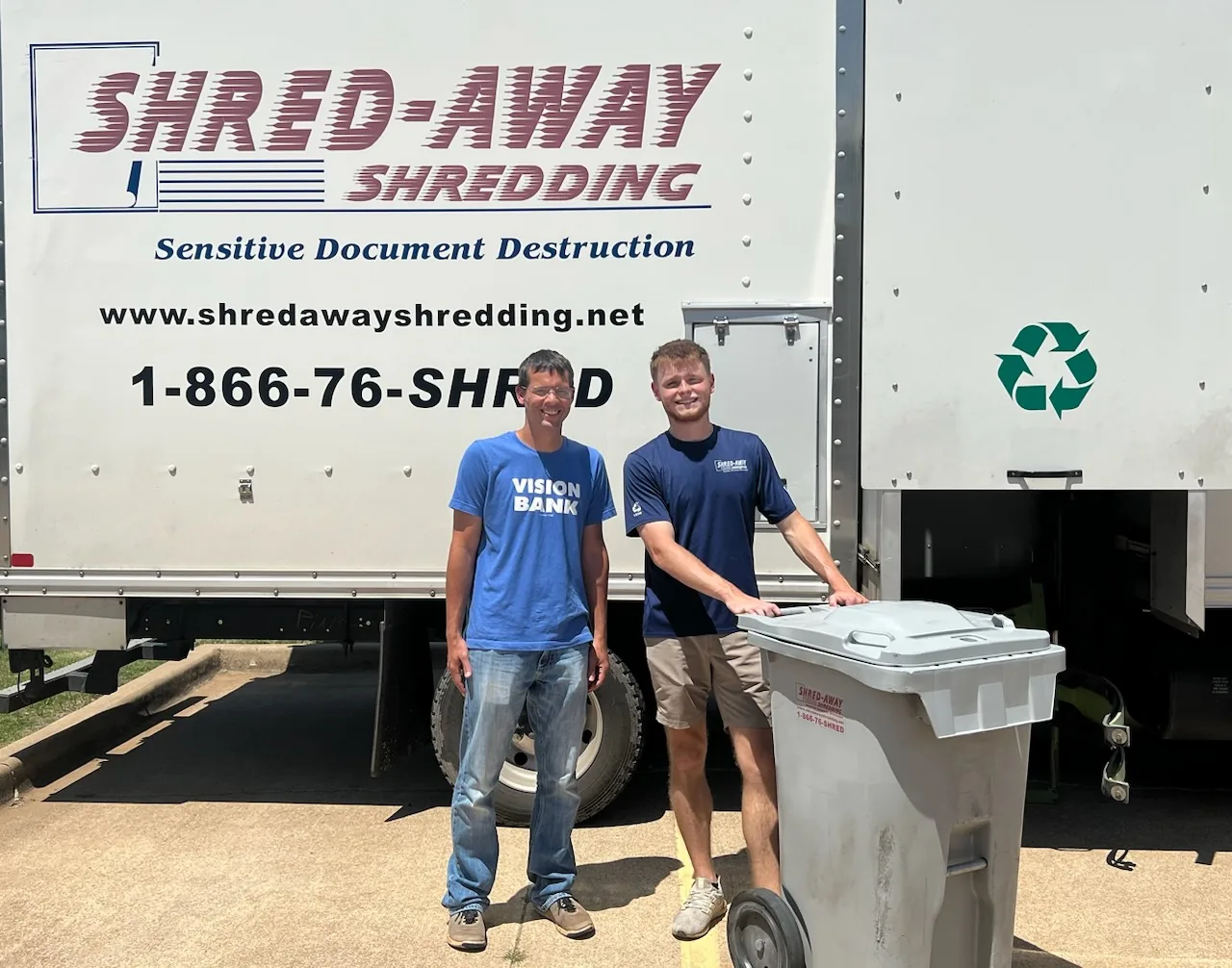 Two Shred-Away staff members with a customer beside a shredding truck and a locking bin.