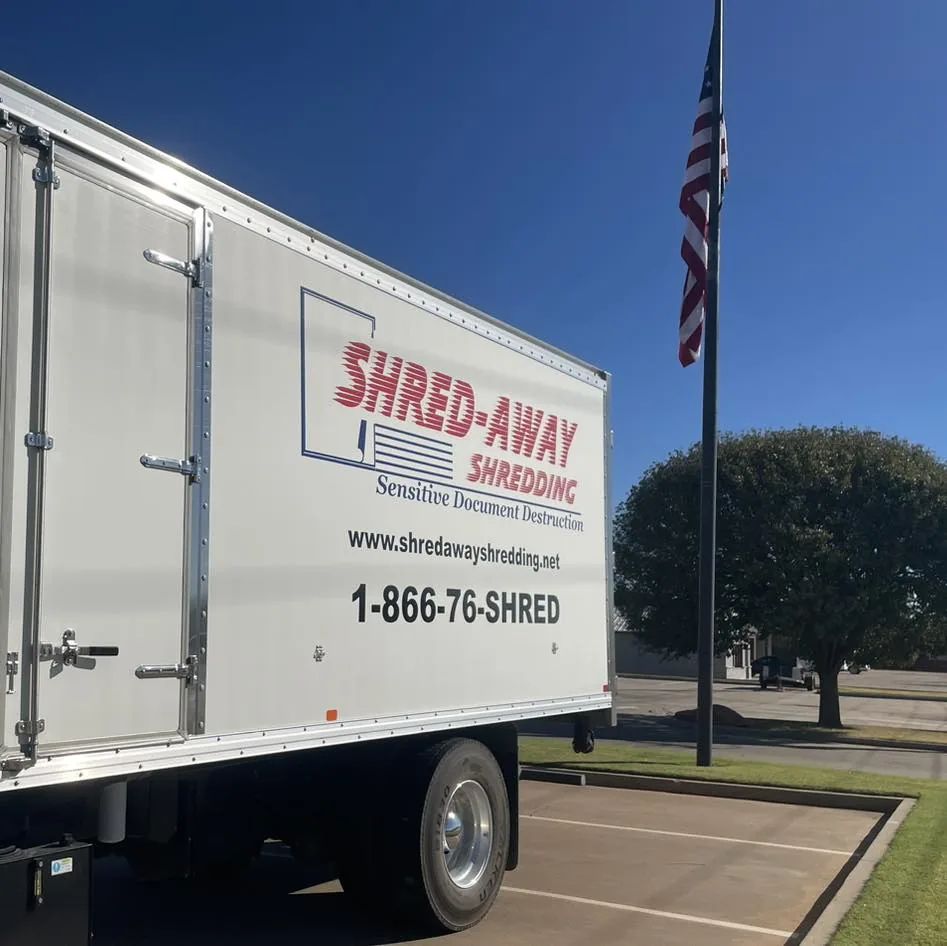 A Shred-Away truck parked beneath an American flag against a clear blue sky.