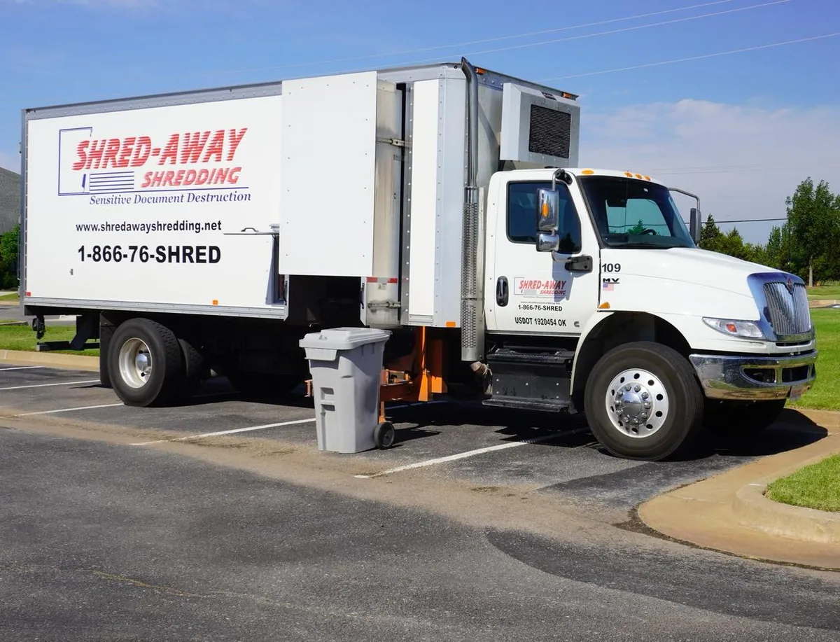 A Shred-Away truck with its lift deployed collecting a bin at a customer site.